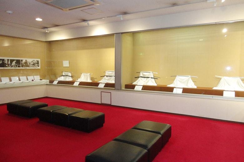 床に赤い絨毯が敷き詰められ、壁側にはガラス張りの展示スペースがある塚本美術館内の写真