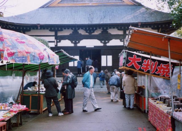 甚大寺の前で催されている縁日に、出店が並んでおり、買い物にお客さんが訪れている写真