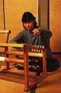 畳の部屋に置かれた織機で作品を制作している久田美智子さんの写真