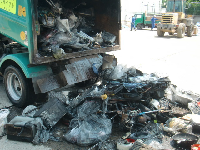 ゴミ収集車の中で燃えて黒く焦げたごみの一部が荷台から降ろされている写真