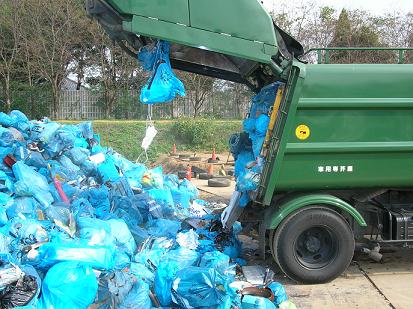 最終処分場への搬入された大量の埋め立てごみと緑色のゴミ収集車の写真