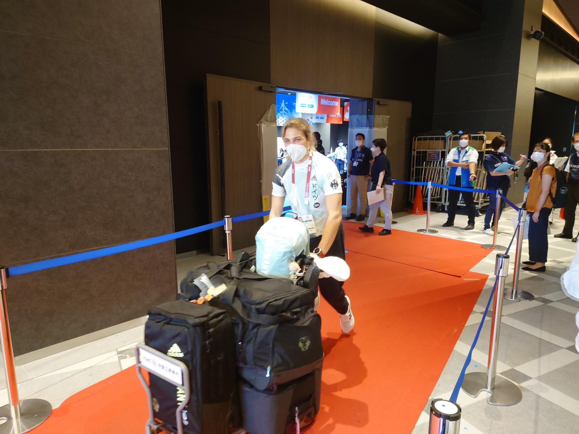 アナ・シェル選手が、赤いカーペットの上を、荷物をたくさん載せたカートを押している写真