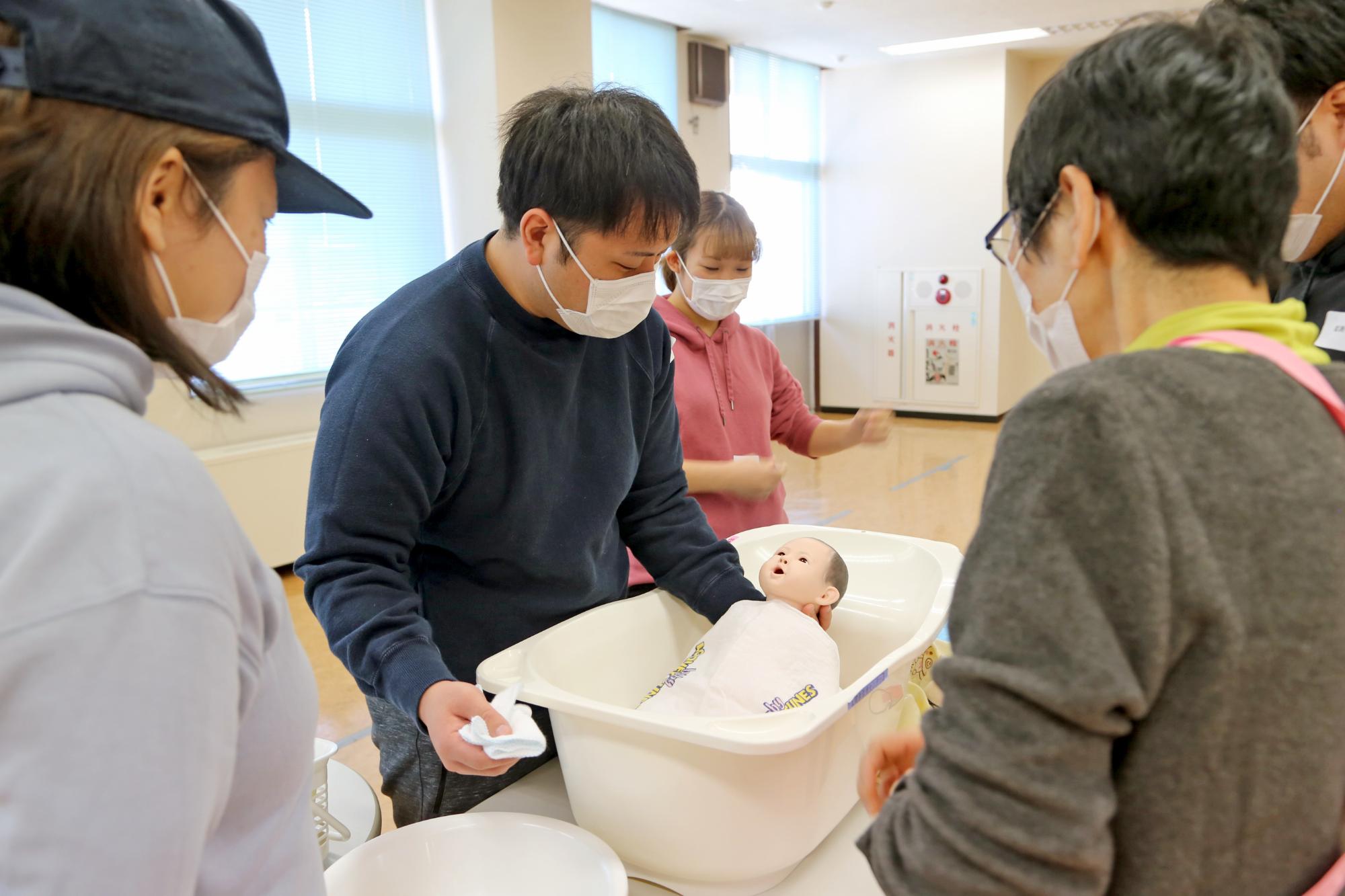 赤ちゃんの人形を使って沐浴体験をしている参加者の男性の写真