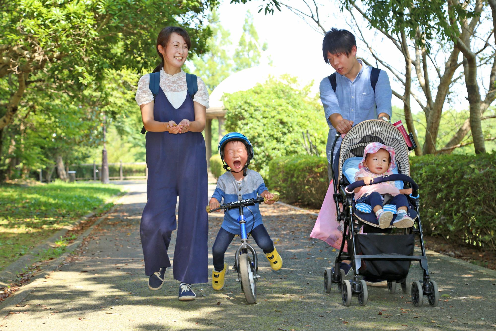 緑道を三輪車に乗った男の子、赤ちゃんの乗ったベビーカーを押すお父さん、お母さんが歩いている写真