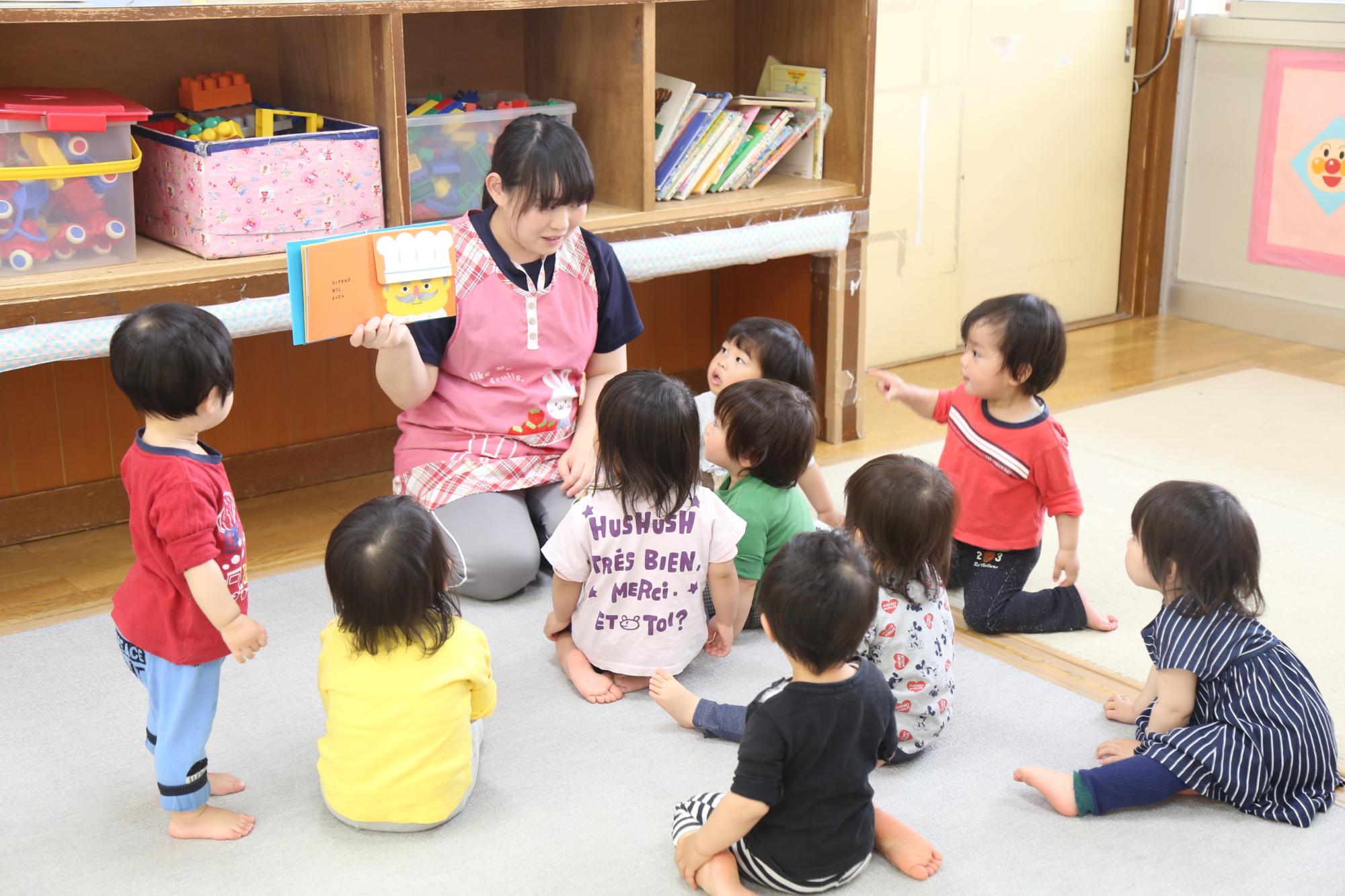 絵本を持った保育士の周りに園児たちが集まって座っている写真