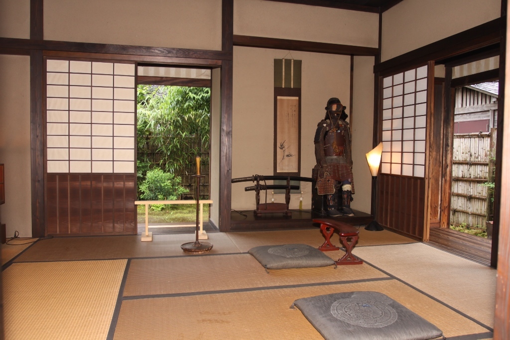 畳の敷かれた和室で、床の間に甲冑や刀が飾られ、壁には掛け軸が掛けられている室内の写真