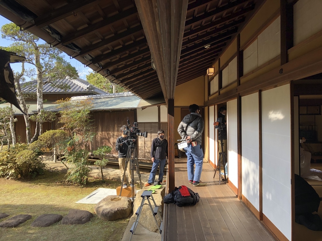 庭園に設置したカメラで室内を撮影しており、数名のスタッフが縁側に立ち、室内での演技を見守っている撮影風景の写真