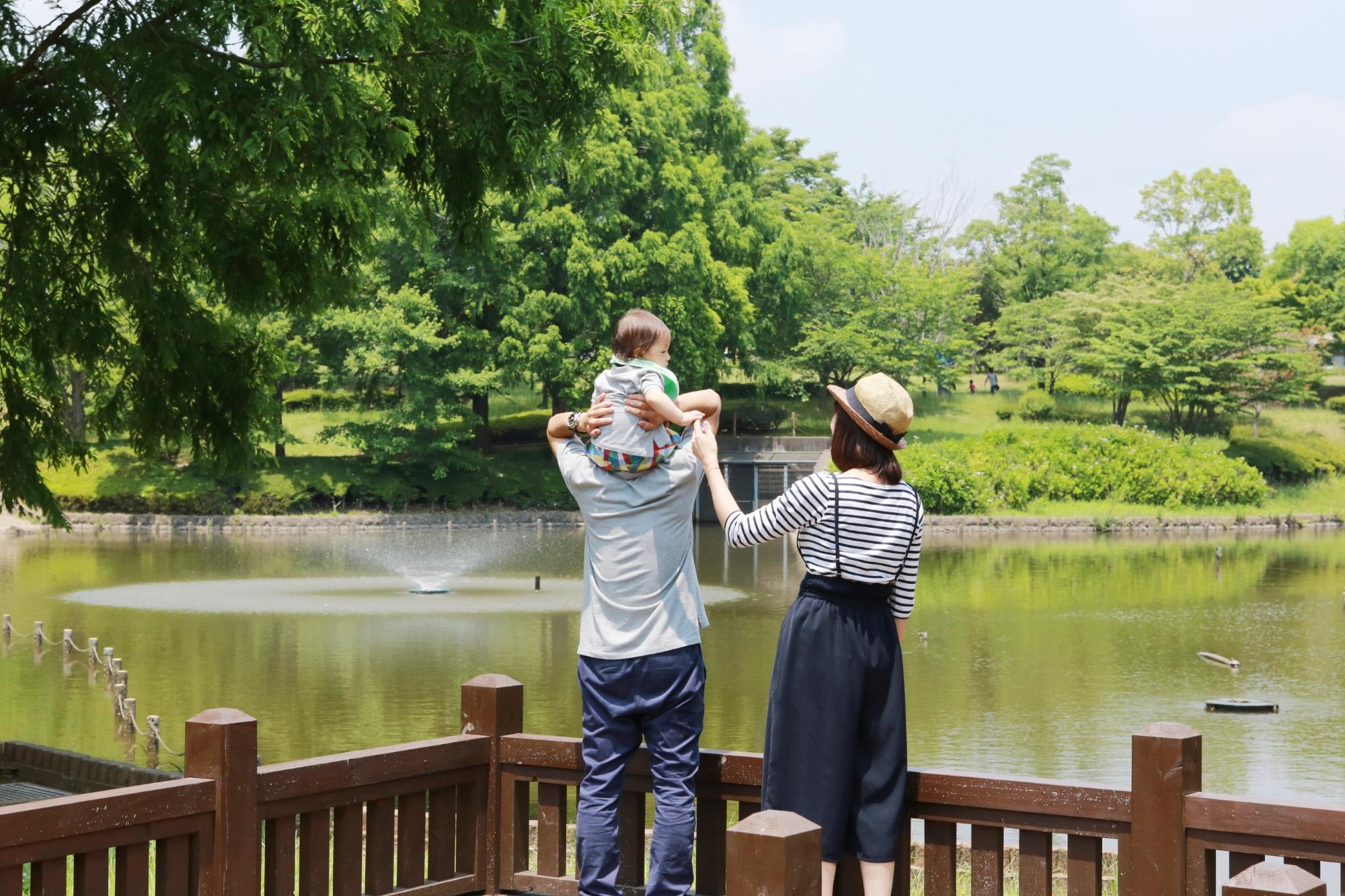 手前に赤ちゃんを肩車したお父さんと、お母さんが立っていて、奥に池が写っている七井戸公園の写真