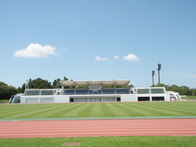 屋根がついた2階建ての観客席と、中央には芝生のフィールド、手前には白線で仕切られたコースが写る競技場の写真