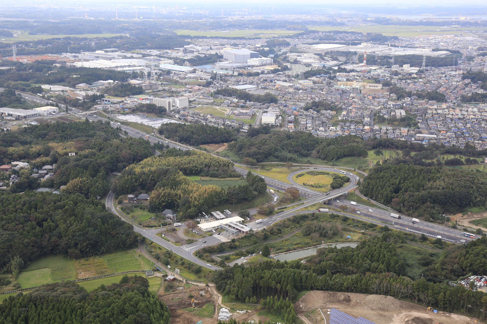 奥には住宅地、手前には森林、中央にカーブした道路が写っている佐倉インターチェンジを上空から写している写真