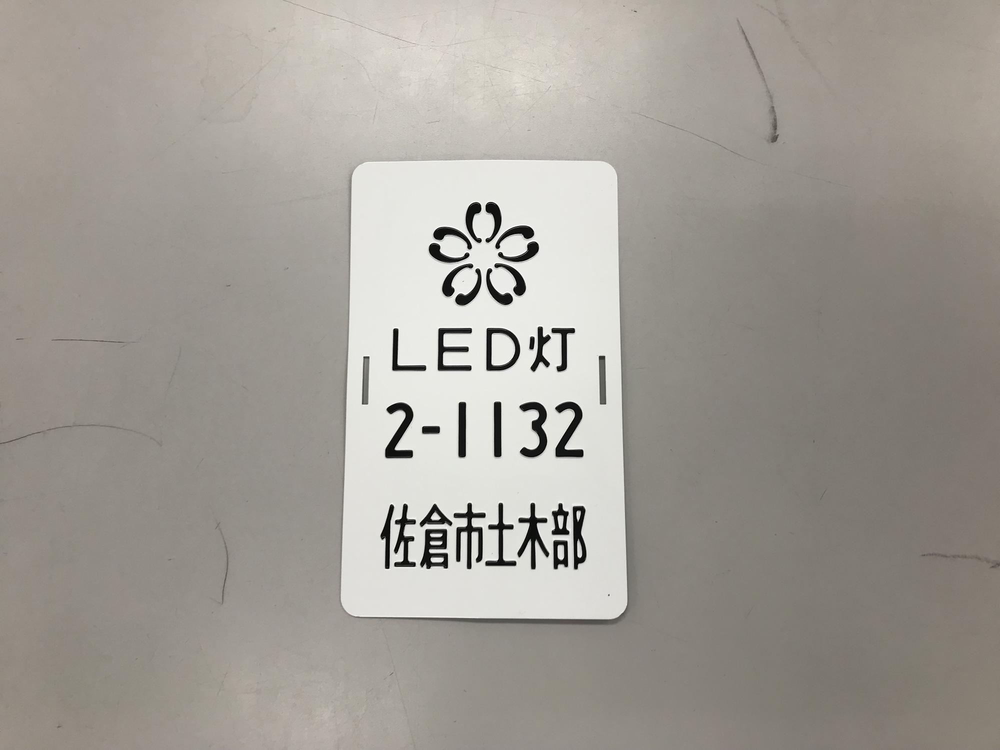 白地に黒でLED灯2-1132佐倉市土木部と書かれた街路灯ナンバープレートの写真
