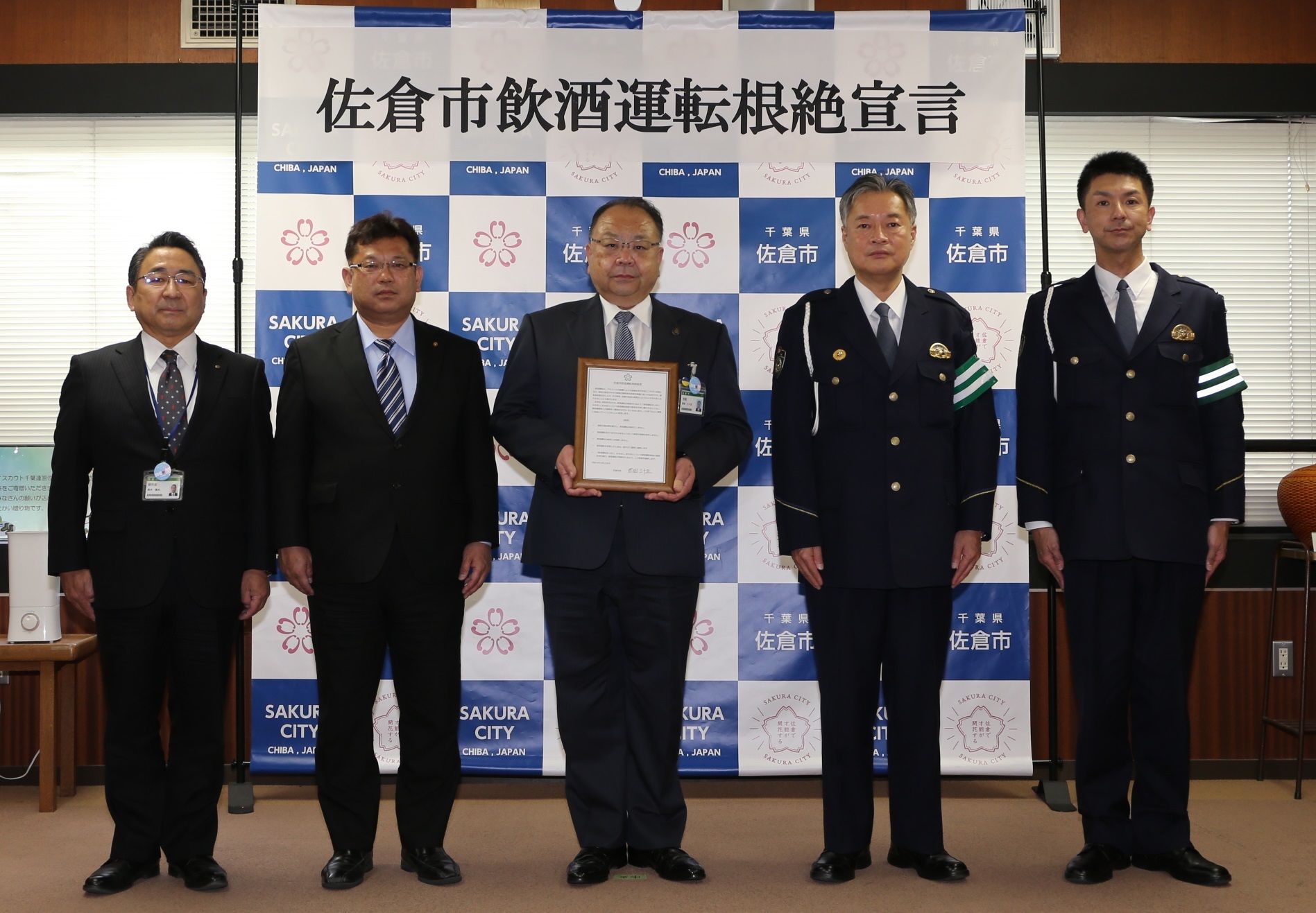 左からスーツ姿の男性が3人、制服を着た警察官2人の5人が横並びで立ち、中央の西田市長が佐倉市飲酒運転根絶宣言書を持っている写真