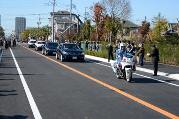 開通した道路を白バイの先導による走り初めが行われ道路脇で数名の人達が写真を撮っている写真