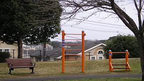 左側にベンチ、右隣に階段昇降とぶら下がりなどのできるオレンジ色の健康遊具が設置された飯重1号近隣公園の写真