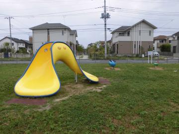 住宅街に隣接した園内に、スプリング遊具や黄色の変わった形のすべり台が設置されている写真