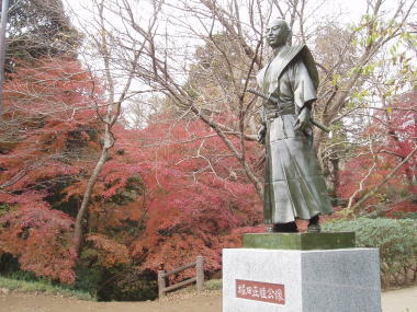 紅葉をバックに、斜めから撮影した堀田正睦公の銅像の写真