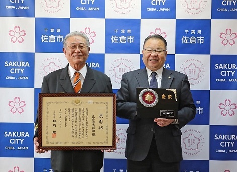 表彰楯を持っている市長と額に入った表彰状を持っている男性が横に並んで記念撮影をしている写真
