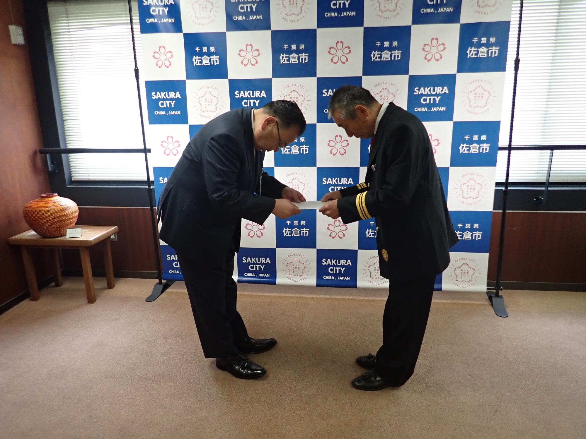 お互いにお辞儀をして事例の授受を行っている西田市長と齋藤団長の写真