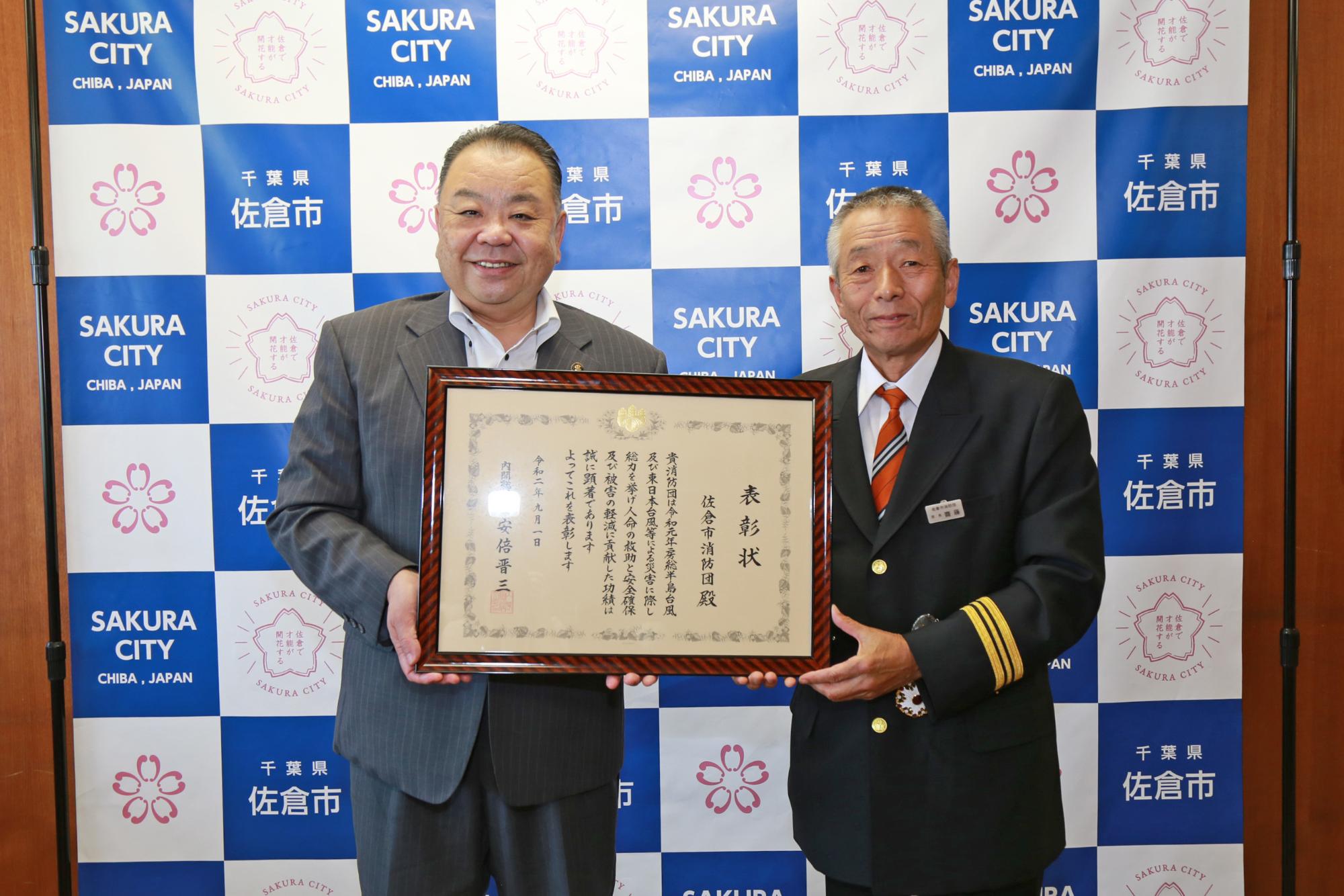 齋藤消防団長と西田市長が額縁に入った表彰状を一緒に持ち記念撮影をしている写真