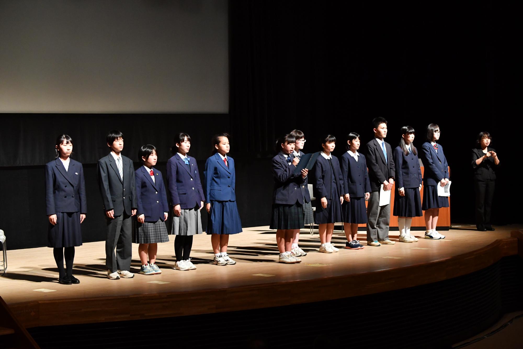 ライトアップされた舞台に並ぶ制服を着た男女学生の写真