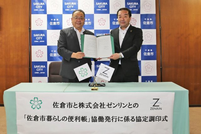 協定調印式で協定書を二人で持って記念撮影を行っている西田市長と吉川支社長の写真