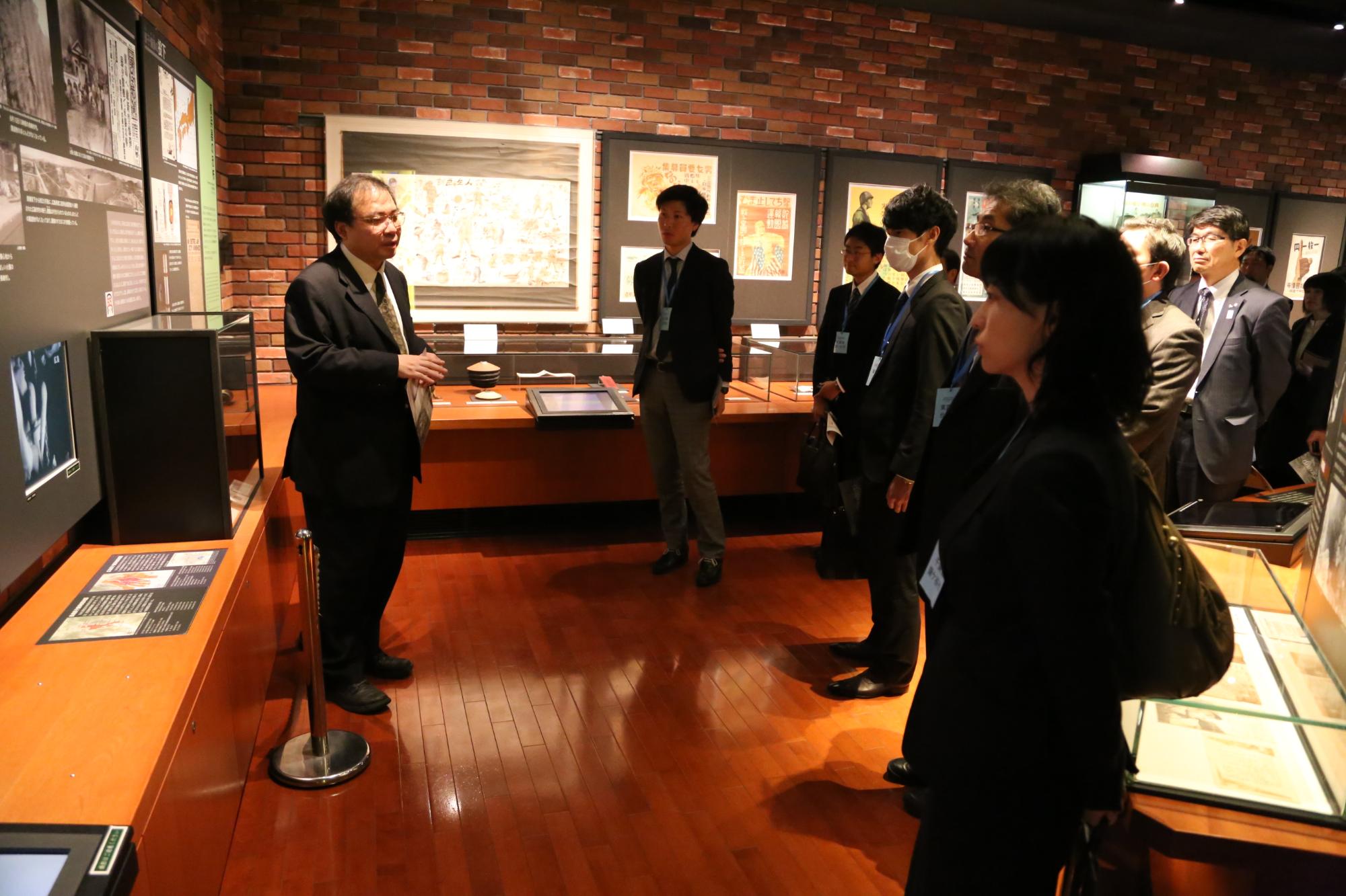 展示品の周りに集まる関係者と、その前に立ち、話をしている男性の写真