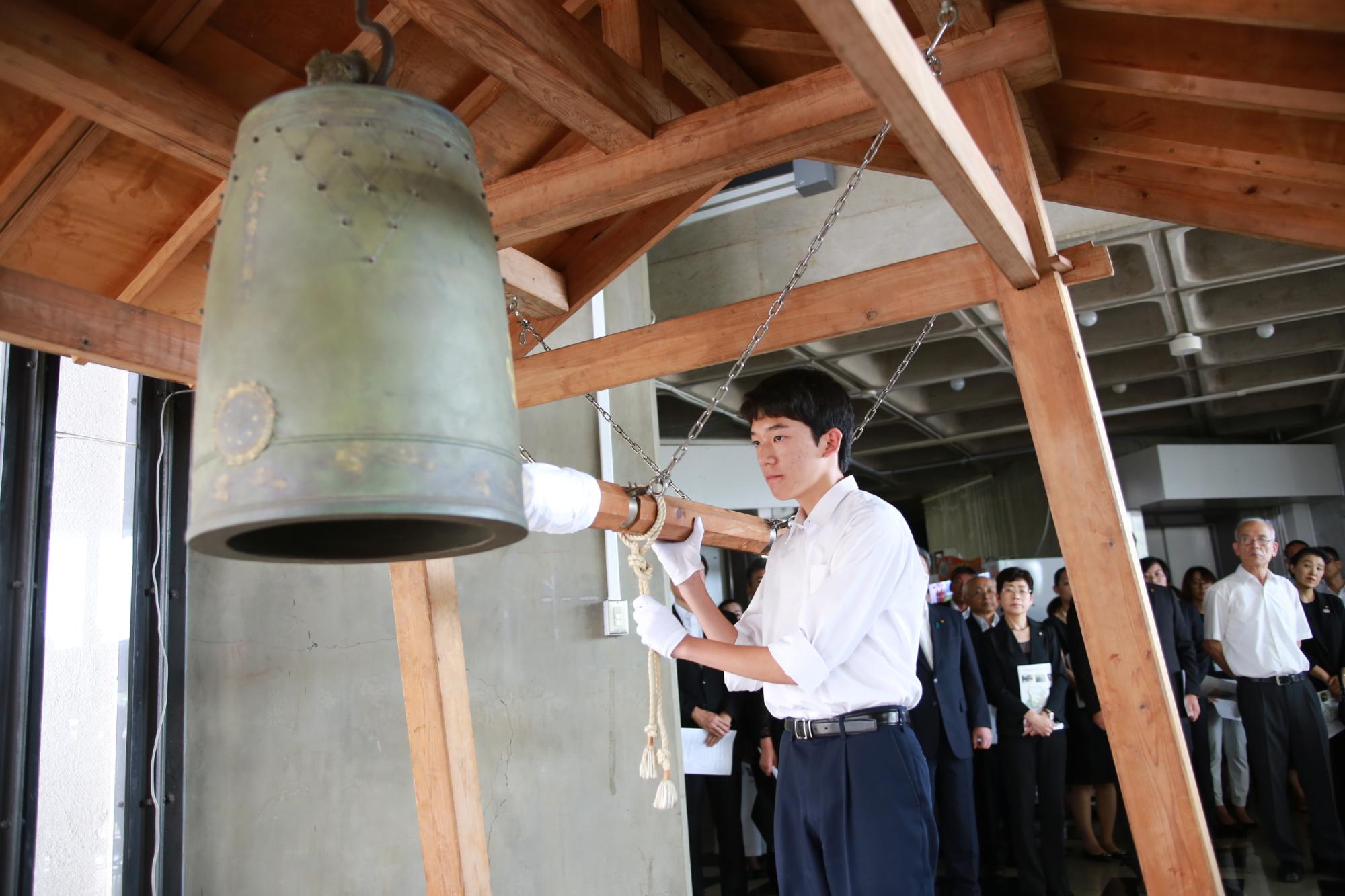 白い手袋をして、桜平和の鐘を鳴らす男性の写真