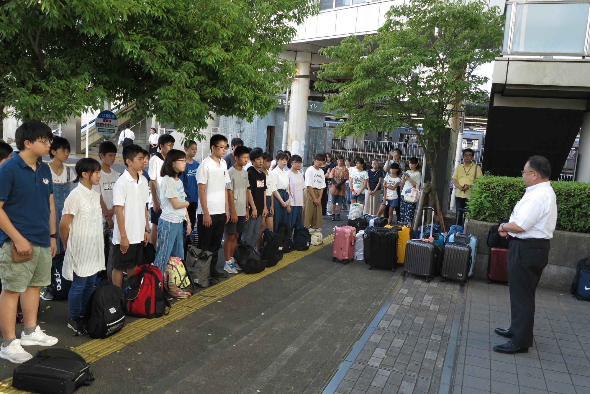 右側に市長、左側には並んで立っている学生たち、中央には沢山のスーツケースが置かれている写真