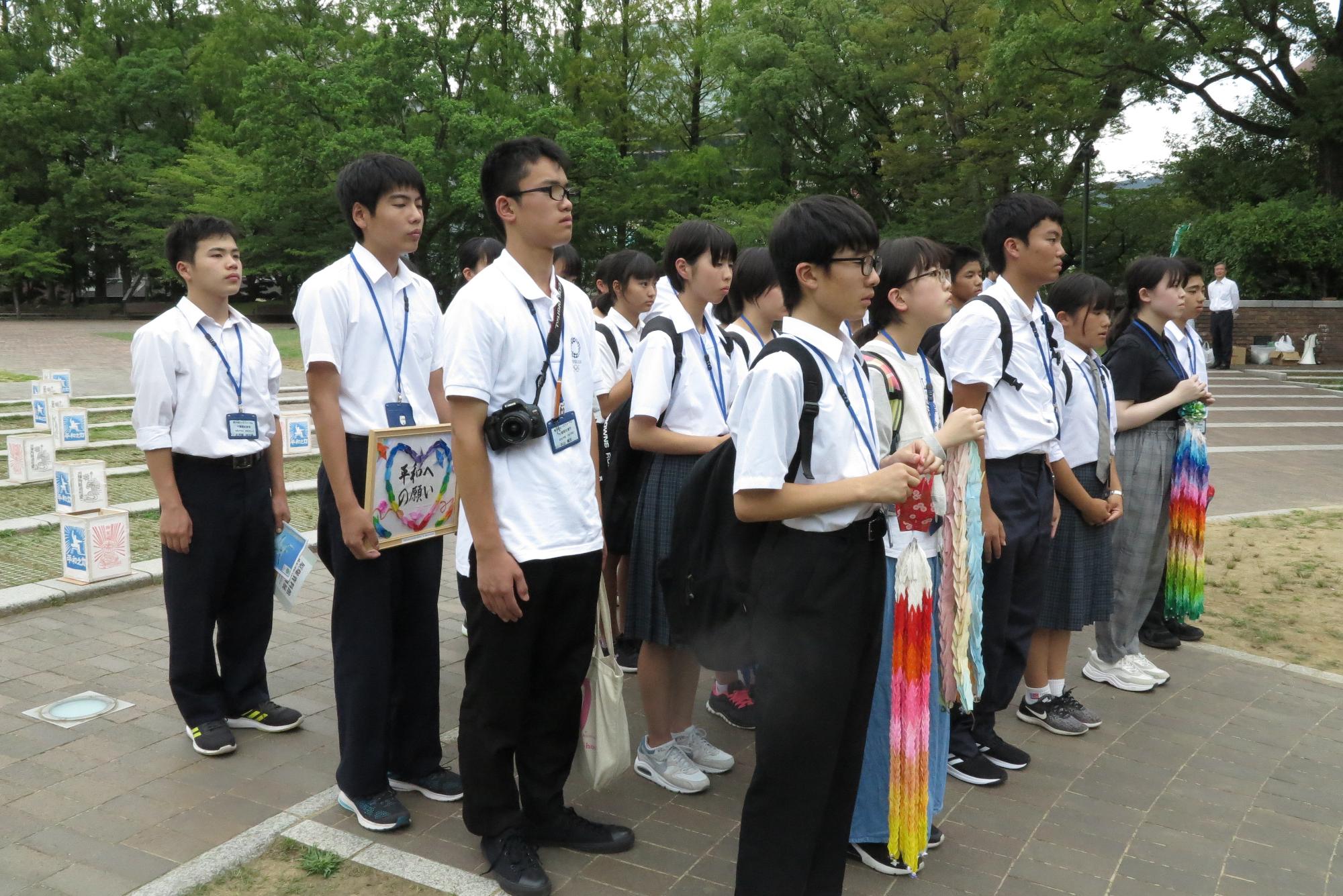 折り鶴やメッセージボードを持った生徒たちが並んで立っている写真