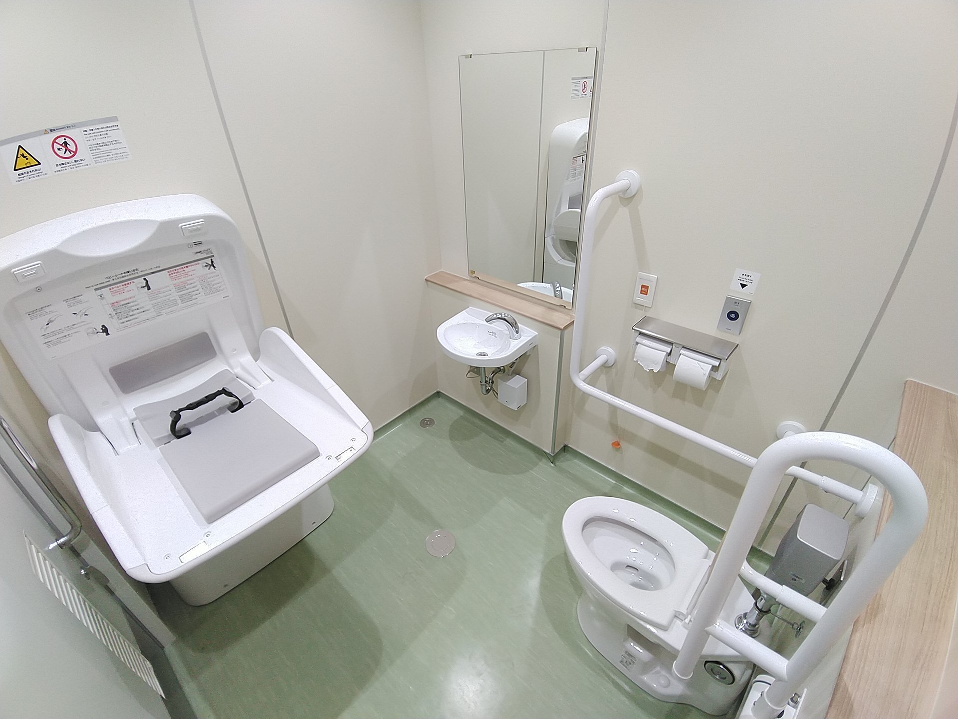 おむつ交換台や手すりつきの洋式トイレ、洗面台の上に鏡が設置されている多機能トイレの写真