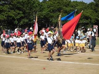 小学生たちが体操服を着て団旗を掲げて行進している写真