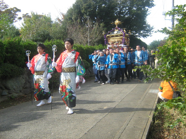 金棒をつとめる女装束の独身男性2人の後ろを神輿を担いだ男性達が歩いている写真