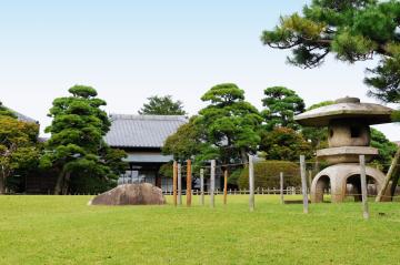 綺麗に整備された芝生の庭園に石灯篭や松の木が見え、その奥に家屋が見える旧堀田正倫庭園の写真