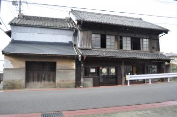 道路横に建つ2階建ての古い木造の店舗兼母屋と脇に蔵のある旧平井家住宅の外観写真