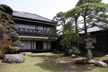 和風庭園の奥に建つ2階建ての白い外壁の旧堀田家住宅の写真
