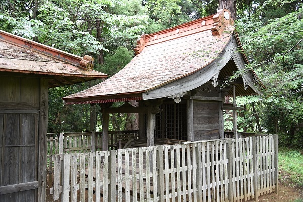 木の板で造られたフェンスで囲われている屋根の朱色が薄くなった大佐倉八幡神社本殿の写真