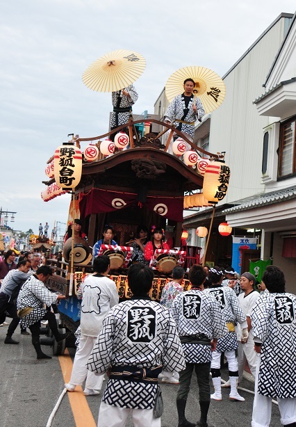 「野狐台町」の神輿の上で和傘を持った2名の男性が立ち、お揃いの法被姿の人達が引き廻しをしている写真