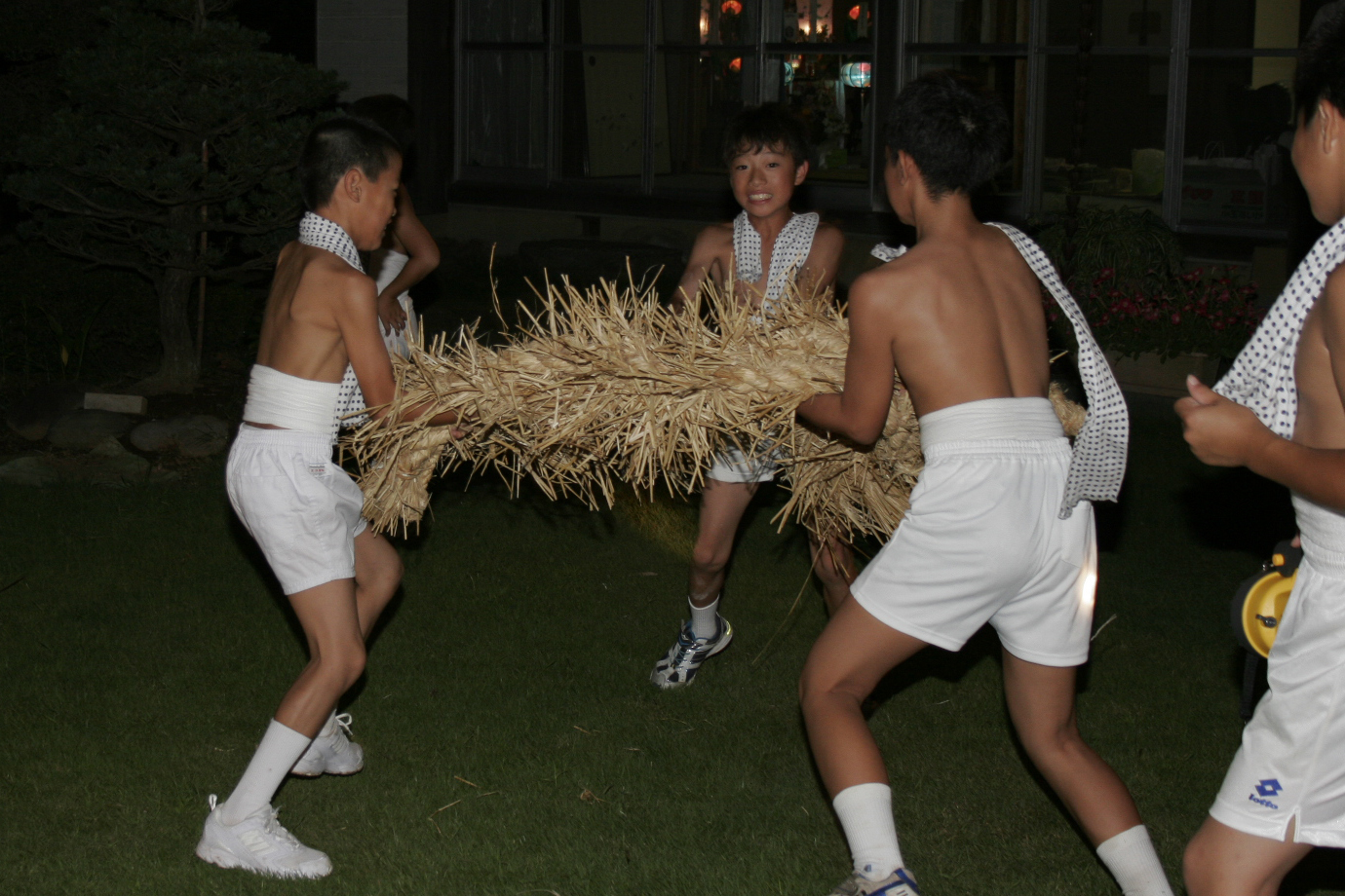 藁で作られた盆綱を3人で抱えている、首に手ぬぐいをかけ上半身は裸で短パンをはいた子供たちの写真