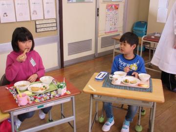 給食を食べる男の子の園児と小学生の女子児童が写っている写真