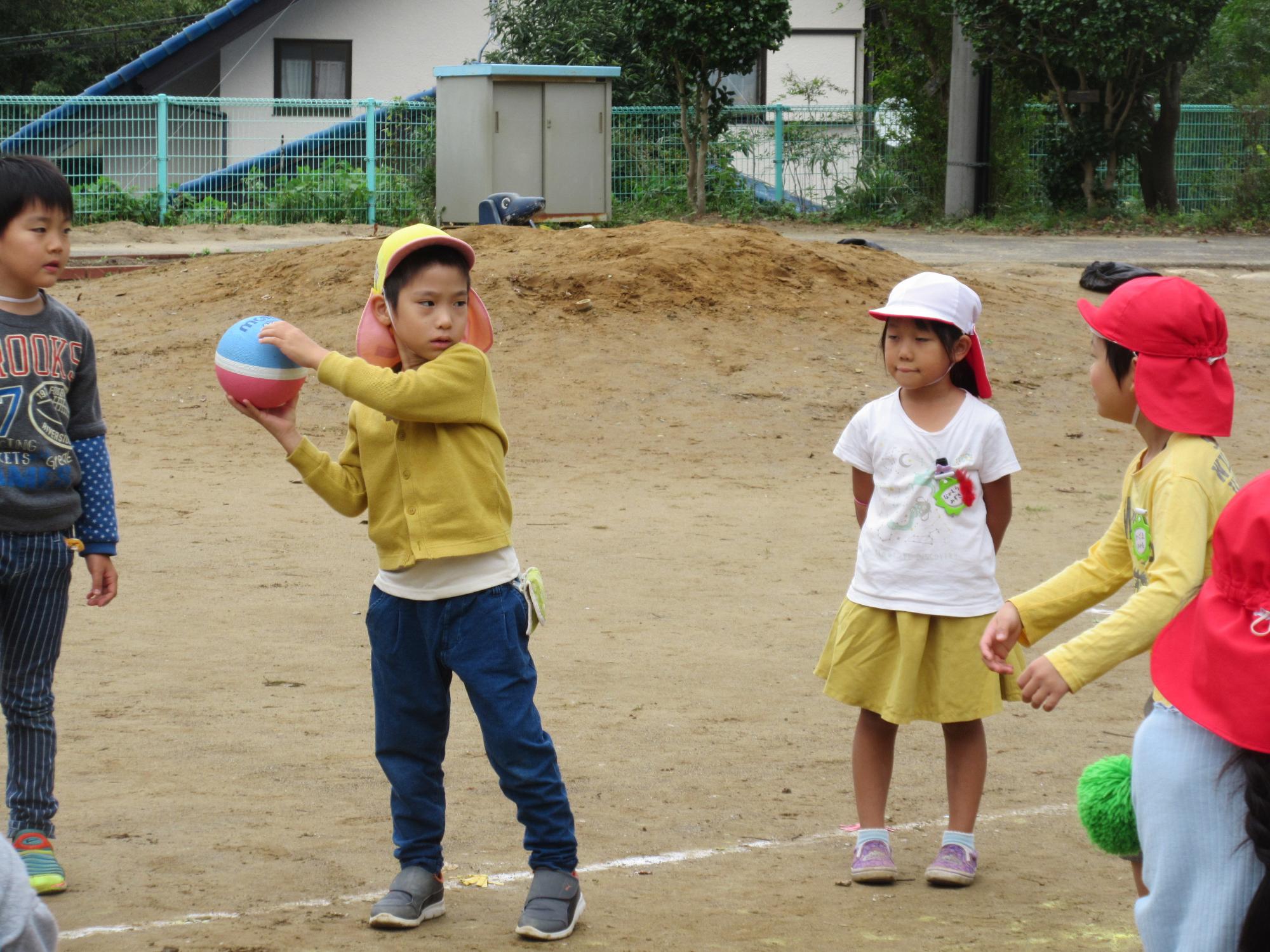 黄色の帽子を被った園児がボールを両手で投げようとしている写真