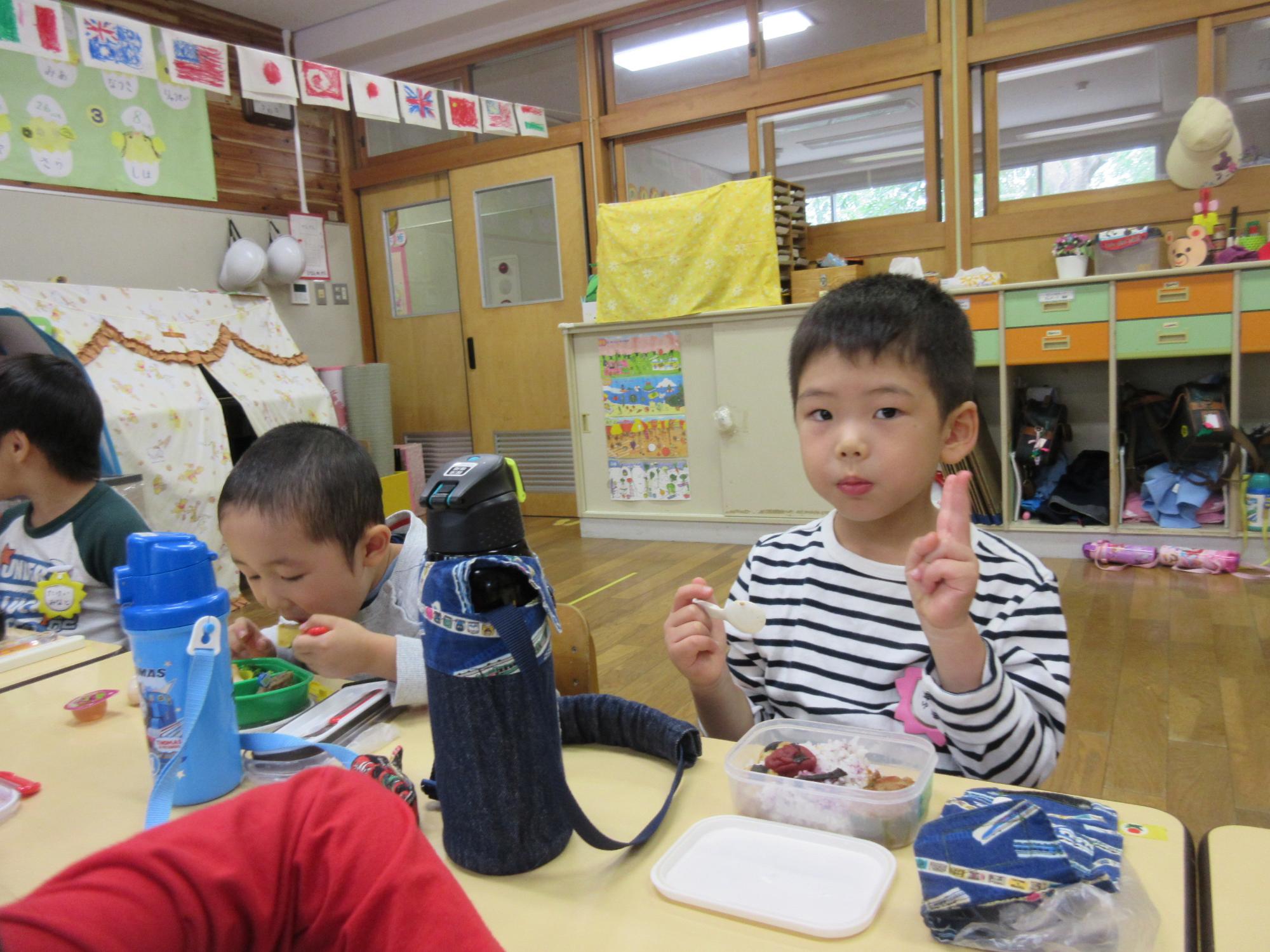 男の子の園児がお弁当を食べながらピースをしている写真