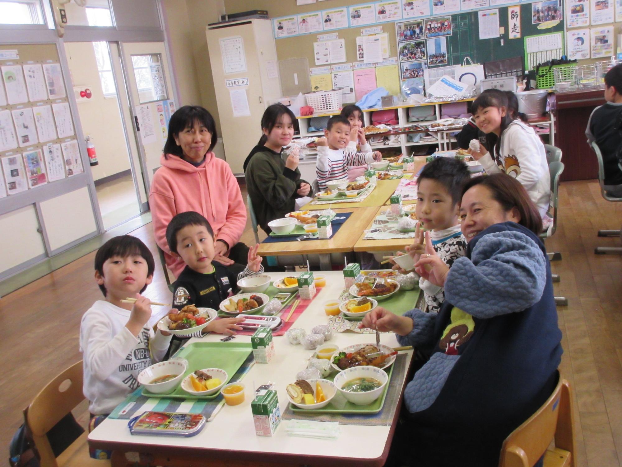 小学校の教室で、給食を食べている園児や児童、関係者が笑顔で笑っている写真