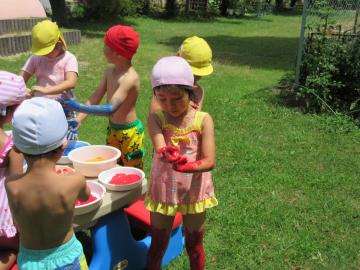水着の園児が、赤や、青い絵の具を手や足につけている写真