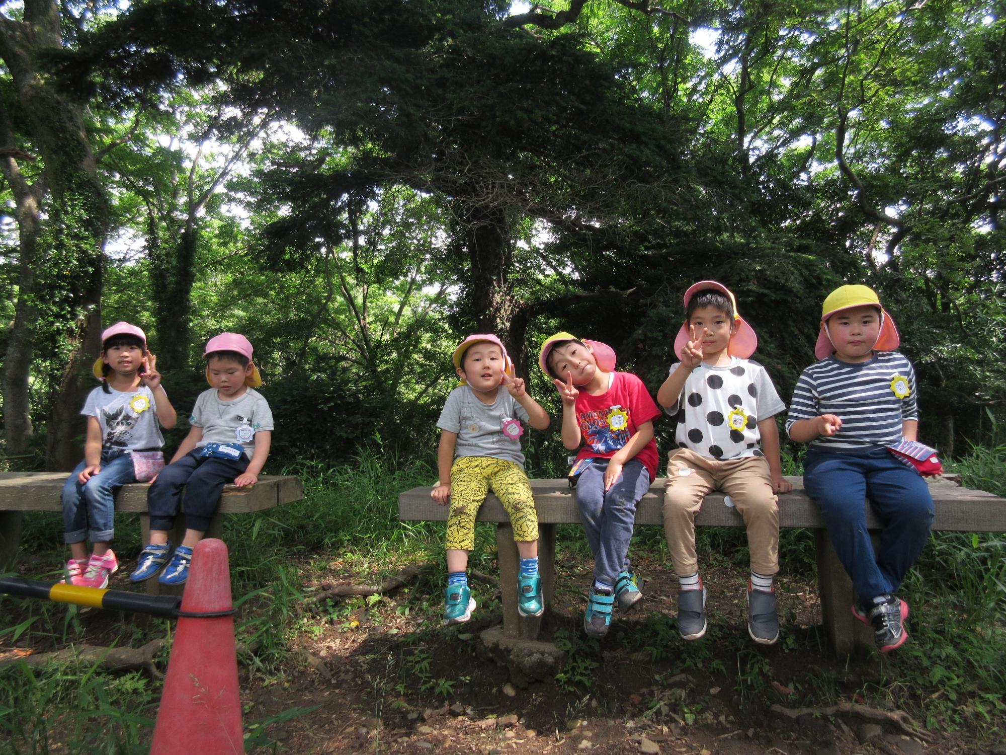 木のベンチに園児たちが座ってピースをしている写真