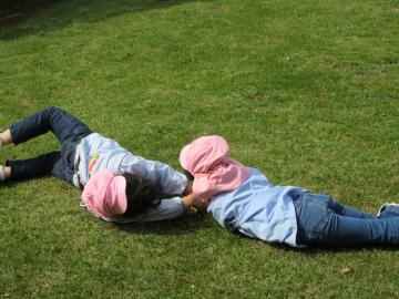 カラーキャップを被った園児2名が、芝生の上で寝転がっている写真