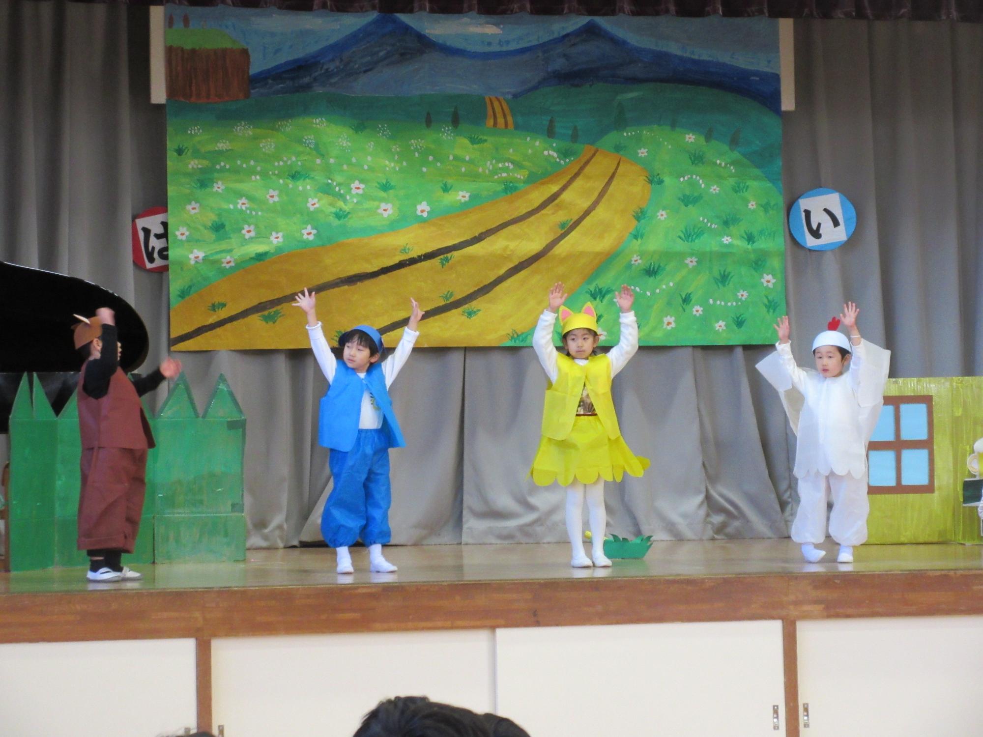 ロバ・イヌ・ネコ・ニワトリの格好をした園児が舞台上に並んで、両手を上げている写真