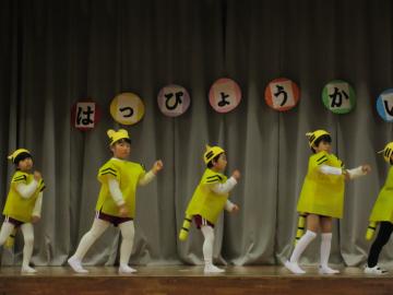 舞台上で黄色のしまじろうの衣装を着た園児たちが踊っている写真