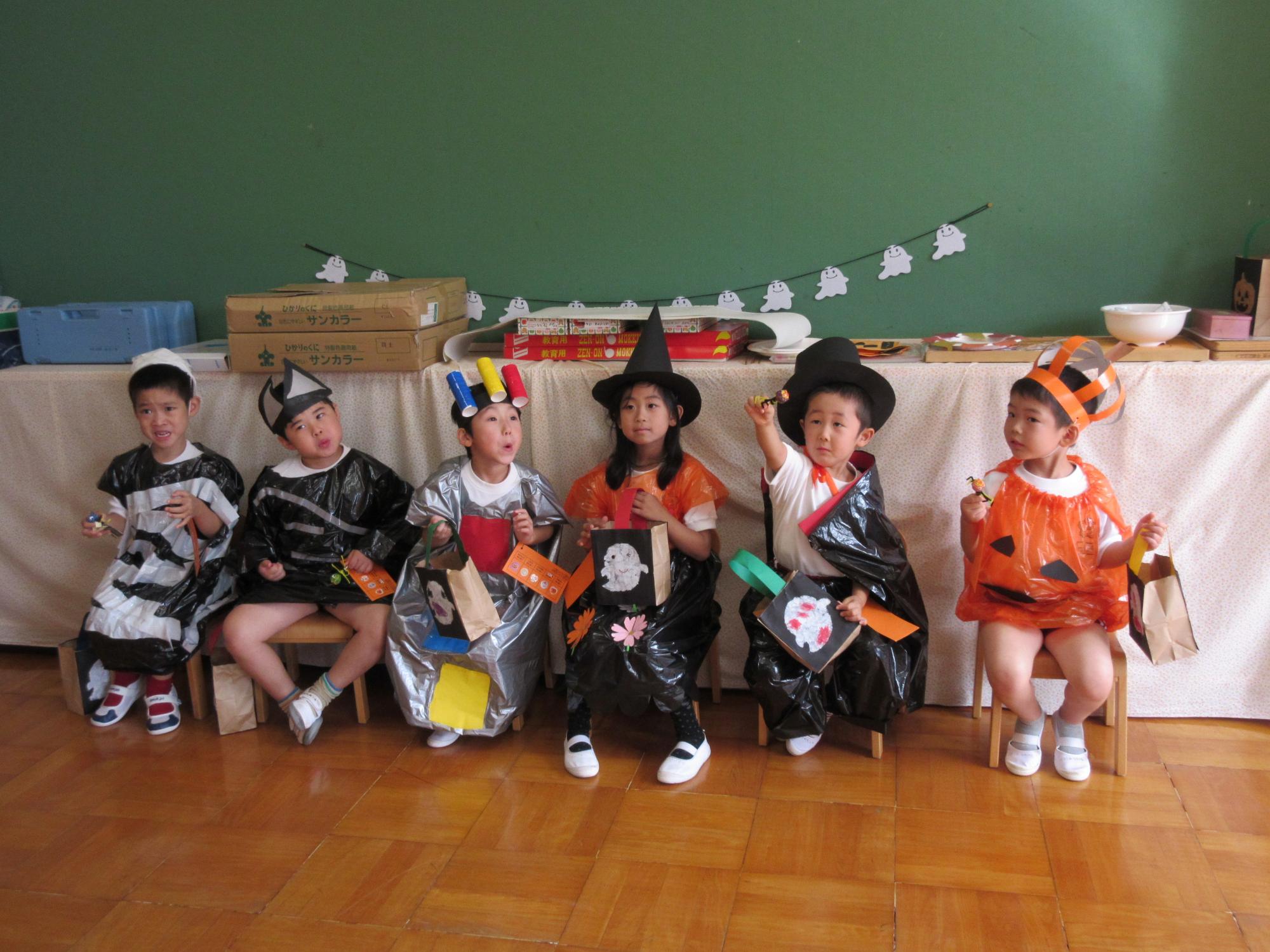 ミイラ男、コウモリ、信号マン、魔女、ドラキュラ、カボチャの恰好をした園児たちが並んで座っている写真