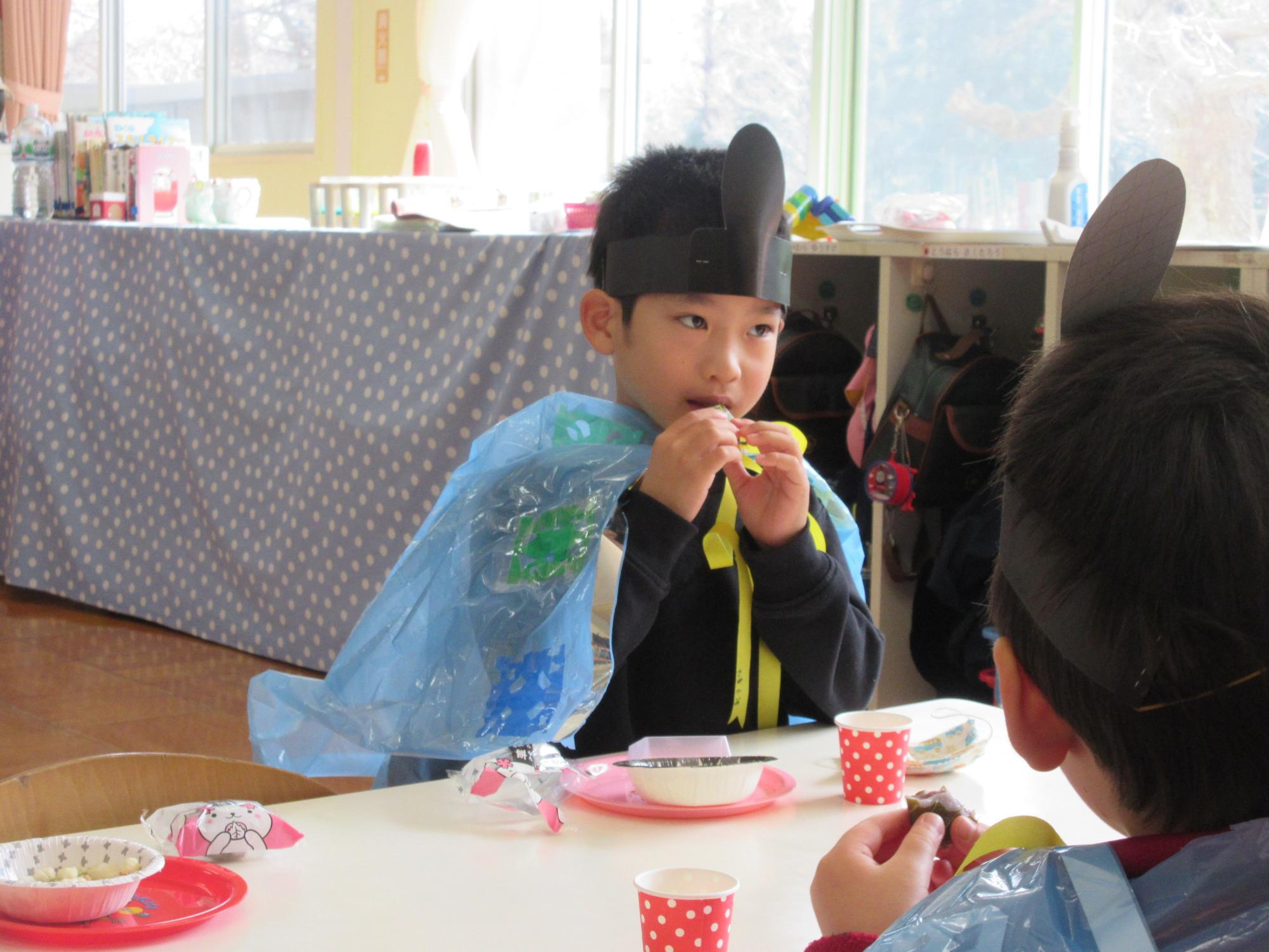机に座っている男の子が両手で桜餅を食べている写真