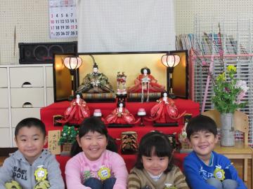 ひな人形の前で年長組の男の子の園児2人と女の子の園児2人が座っている写真